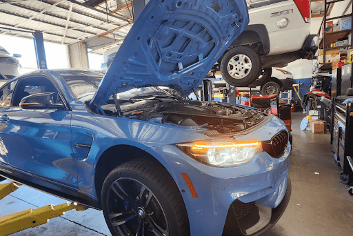 BMW auto repair shop in Van Nuys, CA Los Angeles area. With Sean’s Auto CARE. Image of newer blue BMW vehicle on lift in the shop with lights on and hood open for repair and services.