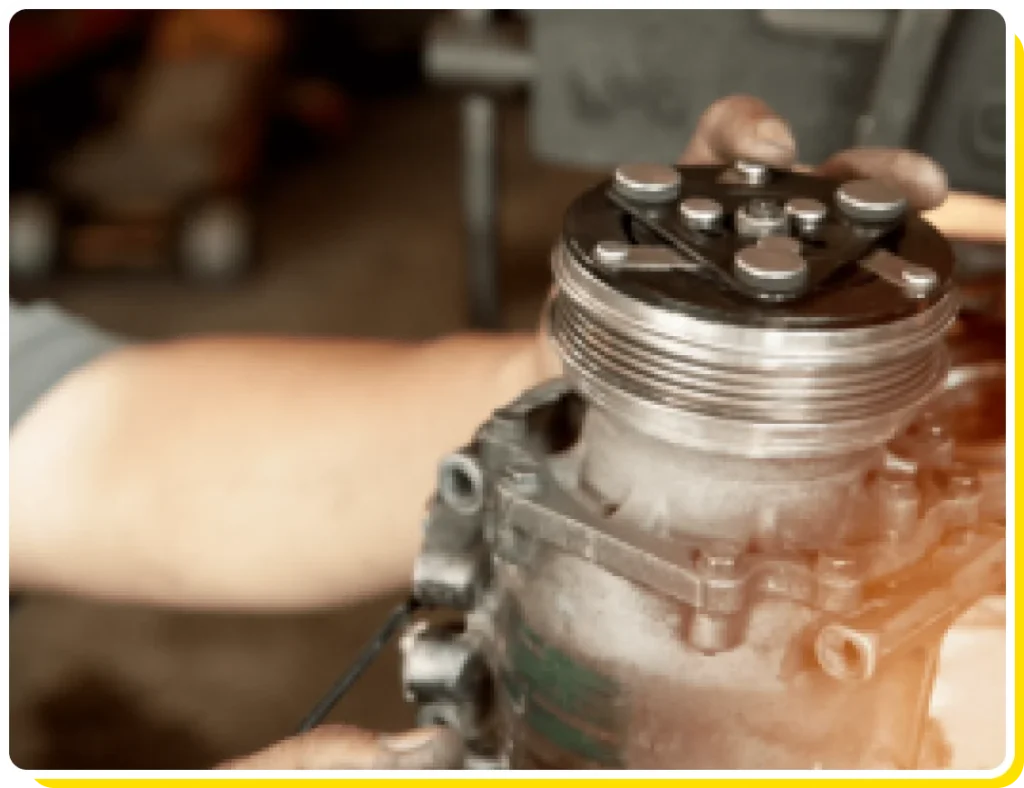 Auto air conditioner repair in Van Nuys, CA. Looking for an auto ac shop near you? Visit Sean's Auto Care. Image of mechanic holding the compressor of an auto ac system that came in the shop for repair.