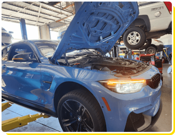 BMW auto repair shop in Van Nuys, CA Los Angeles area. With Sean’s Auto CARE. Image of newer blue BMW vehicle on lift in the shop with lights on and hood open for repair and services.